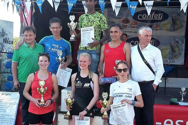 Sieben L&auml;uferinnen und L&auml;ufer stehen auf einer B&uuml;hne mit Pokalen und Urkunden nach einem Wettkampf.