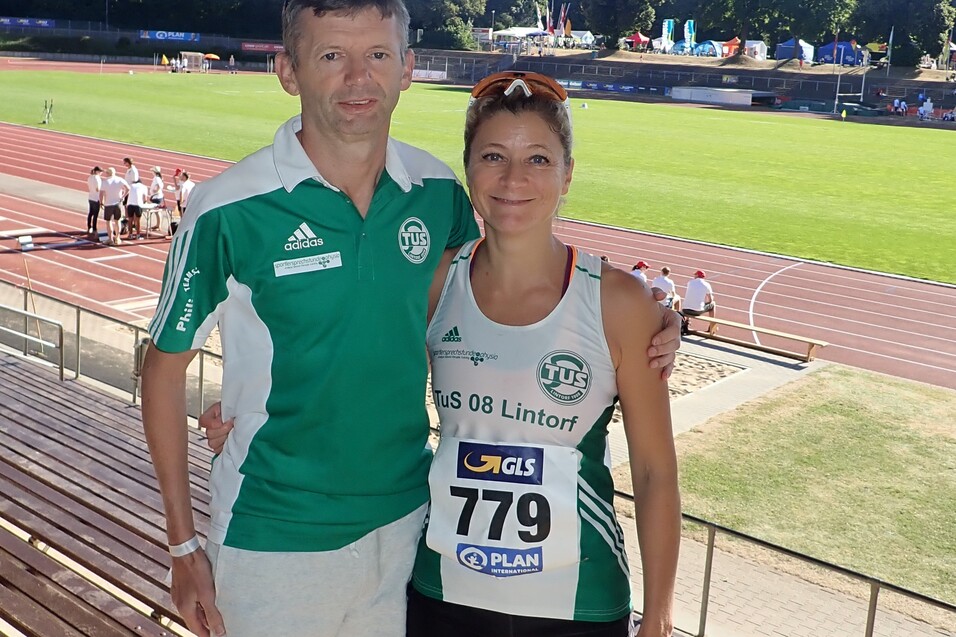 Ein Trainer und eine Athletin in Wettkampfsportbekleidung stehen an der Laufbahn eines Stadions.
