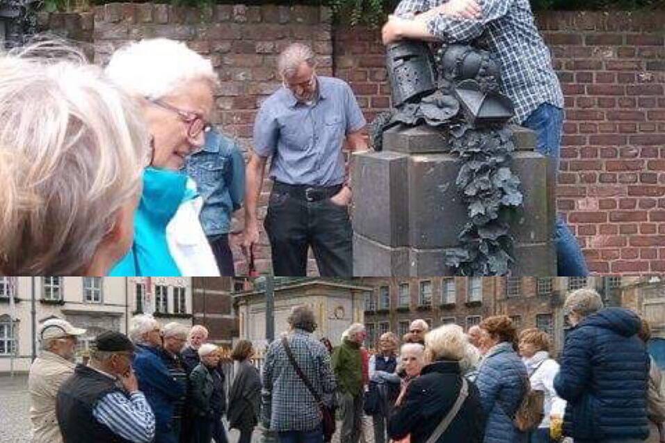 Gruppe von Menschen h&ouml;rt einem Vortragenden zu, der auf einer Statue steht, umgeben von einer historischen Kulisse.