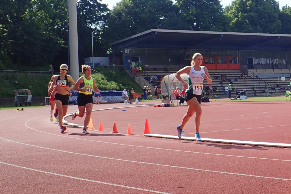 Drei L&auml;uferinnen absolvieren ein Rennen auf einer roten Tartanbahn, w&auml;hrend Zuschauer auf den Trib&uuml;nen sitzen.