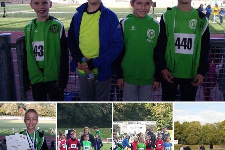 Vier Kinder in gr&uuml;nen Sporttrikots posieren gemeinsam auf einem Sportplatz. Im Hintergrund sind Wettk&auml;mpfe sichtbar.