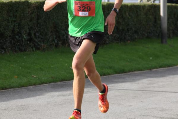 L&auml;ufer mit der Startnummer 329 in gr&uuml;nem Shirt sprintet auf einem Parkweg, umgeben von gr&uuml;ner Vegetation.
