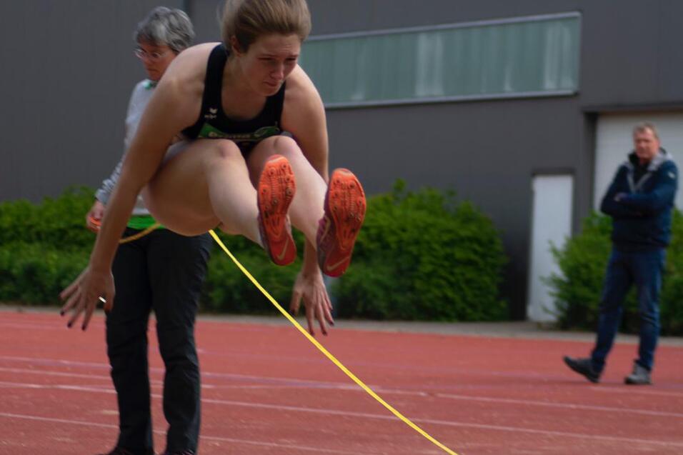 Athletin springt &uuml;ber eine Linie in der Sandgrube w&auml;hrend eines Leichtathletikwettkampfs. Zuschauer im Hintergrund.