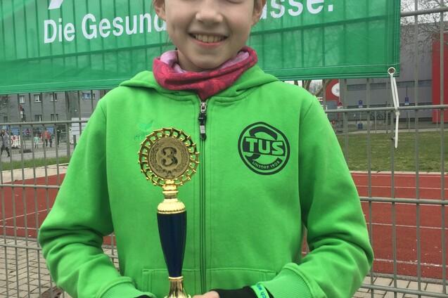 M&auml;dchen in gr&uuml;ner Jacke h&auml;lt einen Pokal vor einer Bannerwand mit dem AOK-Logo.