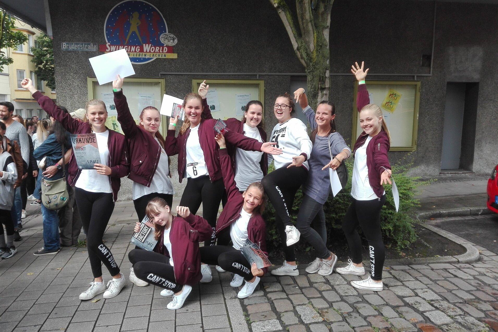 Gruppe junger T&auml;nzerinnen in Trainingskleidung posiert fr&ouml;hlich im Freien, einige halten Urkunden in den H&auml;nden.