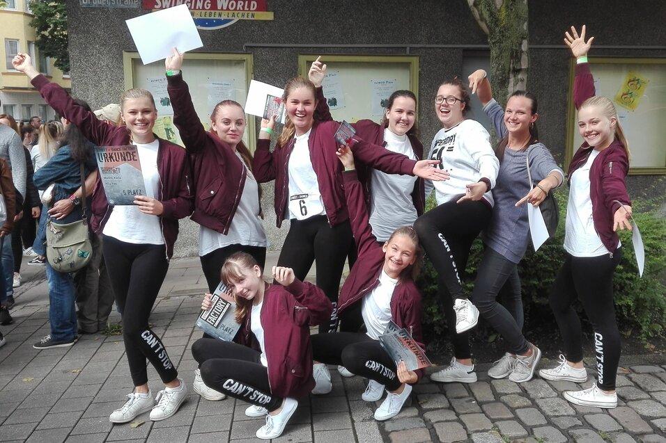 Gruppe junger T&auml;nzerinnen in Trainingskleidung posiert fr&ouml;hlich im Freien, einige halten Urkunden in den H&auml;nden.