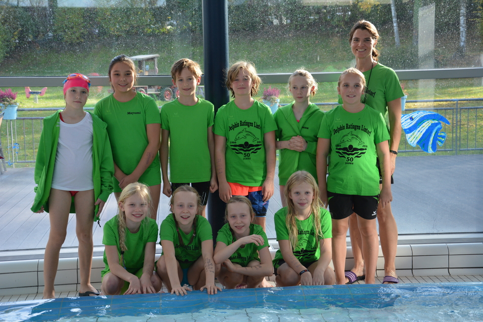 Gruppe von M&auml;dchen in gr&uuml;nen T-Shirts, versammelt vor einem Schwimmbecken, mit einer Trainerin in der Mitte.