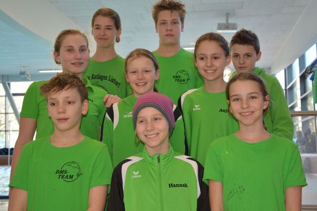 Gruppenfoto von neun Schwimmern in gr&uuml;nen Trikots am Schwimmbecken, l&auml;chelnd und in zwei Reihen angeordnet.