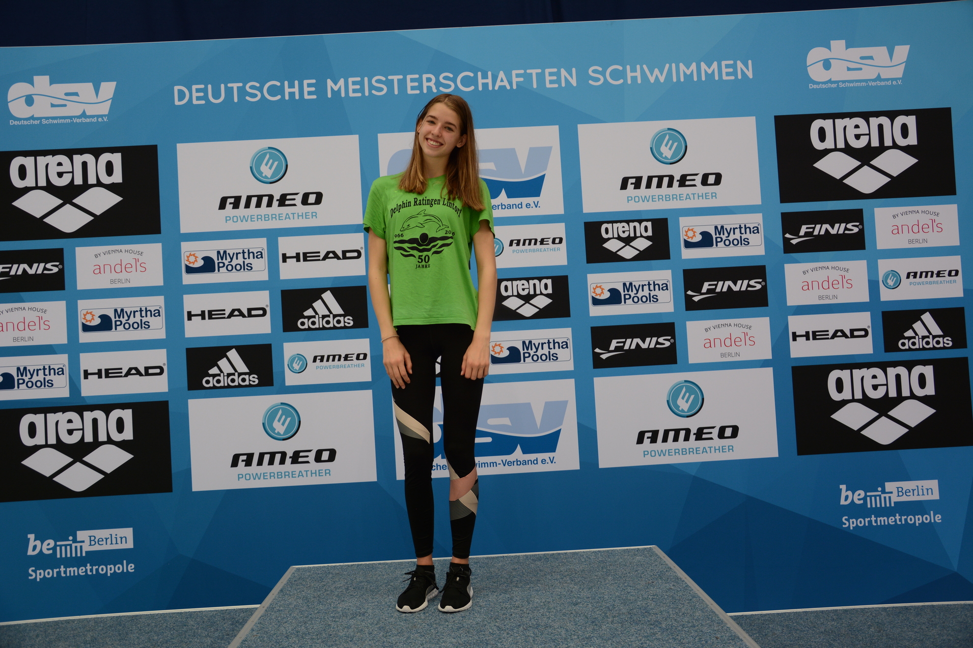 Sportlerin in gr&uuml;nem T-Shirt steht vor einer Sponsorentafel bei den Deutschen Meisterschaften im Schwimmen.