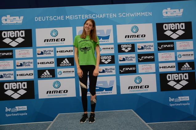 Sportlerin in gr&uuml;nem T-Shirt steht vor einer Sponsorentafel bei den Deutschen Meisterschaften im Schwimmen.