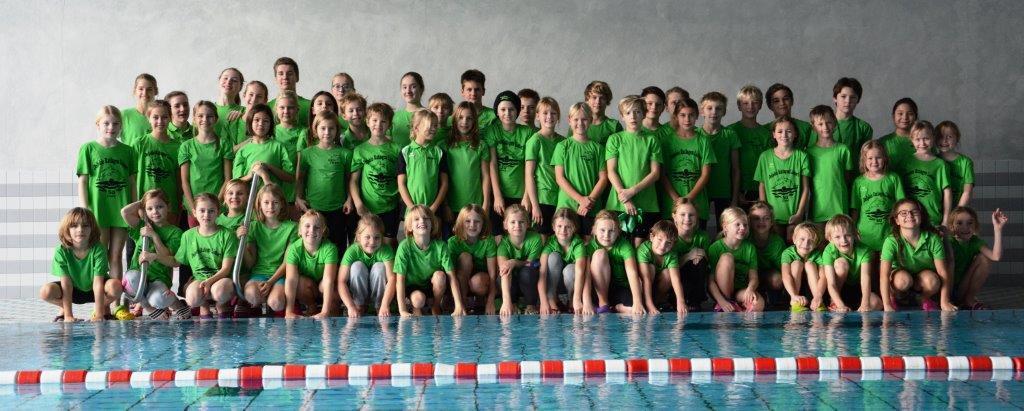 Gruppenshot von 60 Kindern in grünen T-Shirts am Rand eines Schwimmbeckens.