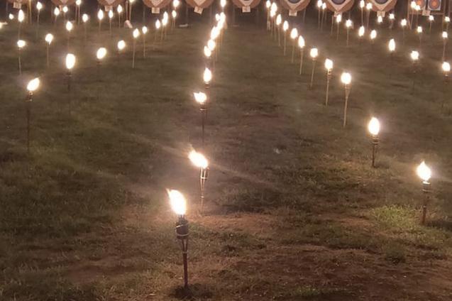 Beleuchteter Bogenschie&szlig;platz mit Zielscheiben und Fackeln in der D&auml;mmerung, umgeben von einem Waldrand.