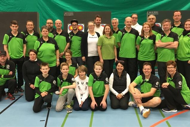 Gruppenfoto einer Tischtennismannschaft in einheitlicher gr&uuml;ner Sportbekleidung, versammelt in einer Sporthalle.
