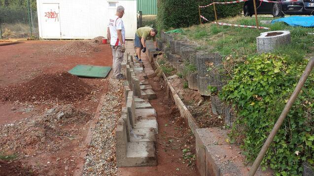 Zwei Männer arbeiten an einer Baustelle, während sie Betonsteine entlang einer Grube verlegen.