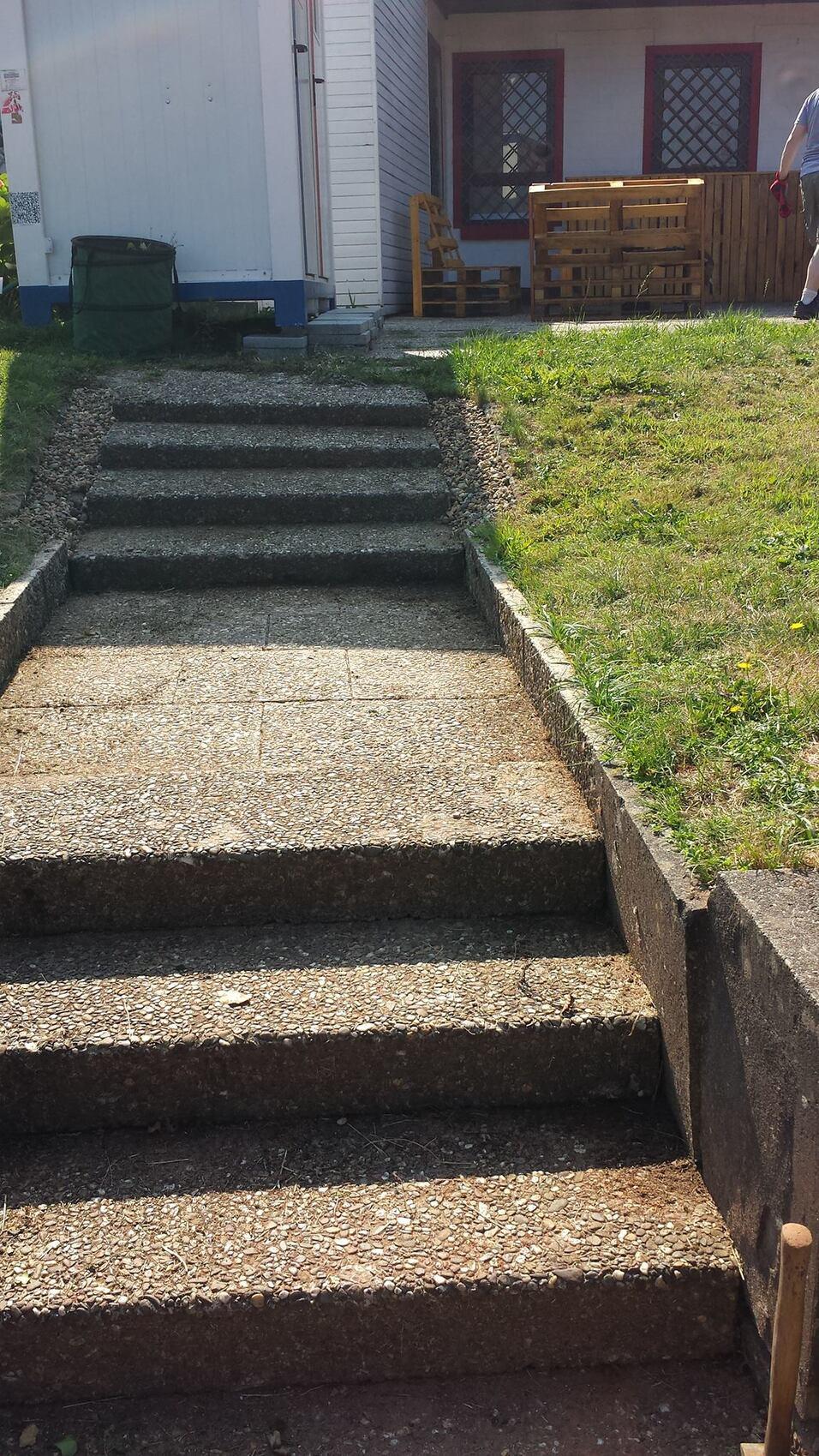 Steinerne Treppe mit mehreren Stufen, die zu einer grünen Rasenfläche und einem Holzgeländer führt.