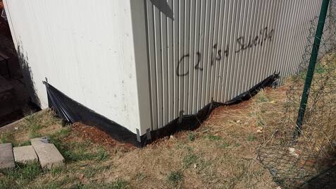 Ecke eines Gebäudes mit grauer Wand, schwarzem Untergrund und dem Graffiti „C2 is Beauty“ auf der Wand.