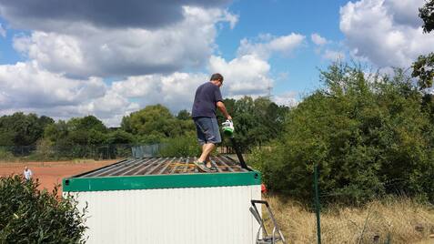 Mann steht auf einem Container und bearbeitet die Oberfläche mit einem Werkzeug unter bewölktem Himmel.