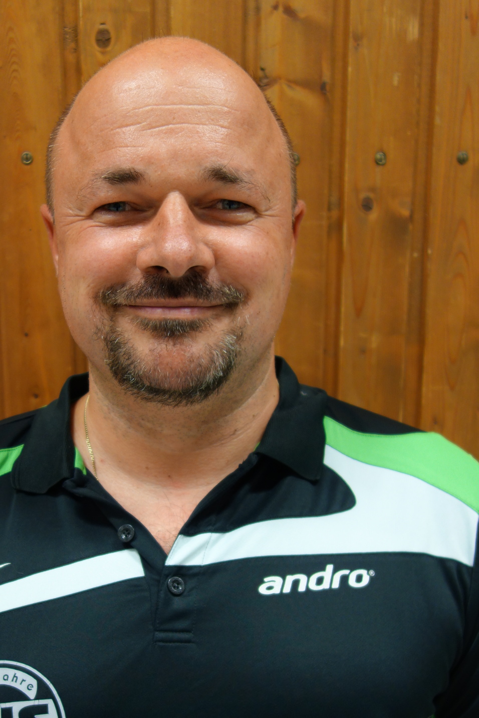 Portr&auml;t eines Mannes mit Glatze und l&auml;chelndem Gesicht, in einem schwarzen Polohemd mit gr&uuml;nen und wei&szlig;en Details.