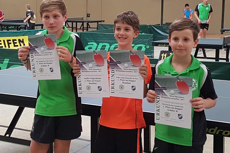 Drei Jungen halten Urkunden und Tischtennisschl&auml;ger in einer Sporthalle mit Tischtennisplatten im Hintergrund.