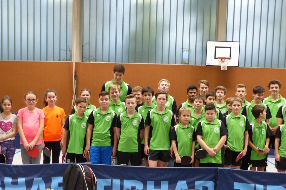 Gruppe junger Tischtennisspieler in gr&uuml;nen Trikots posiert gemeinsam in einer Sporthalle.