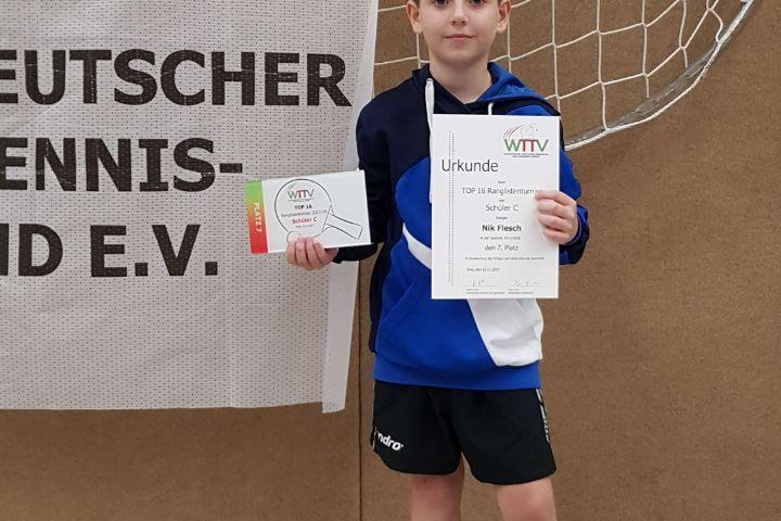 Ein Junge steht vor einem Banner und hält eine Urkunde sowie ein Teilnehmerticket in der Hand.