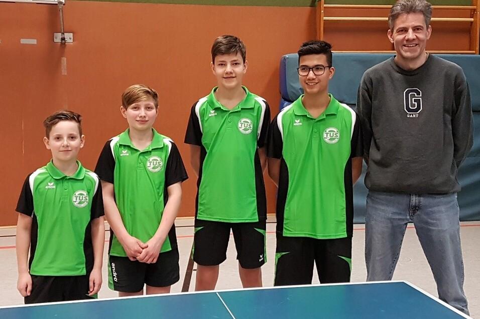 Gruppe von f&uuml;nf Personen in gr&uuml;nen Tischtennis-Trikots stehen neben einem Tischtennistisch in einer Sporthalle.