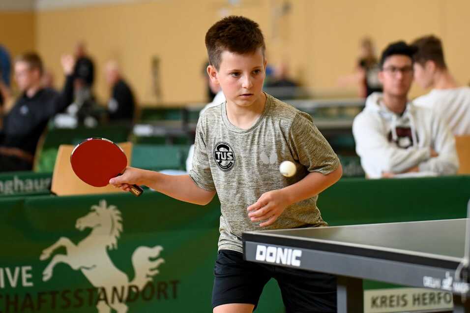 Ein junger Tischtennisspieler bereitet sich mit Schläger und Ball auf einen Schlag an einem Tischtennistisch vor.