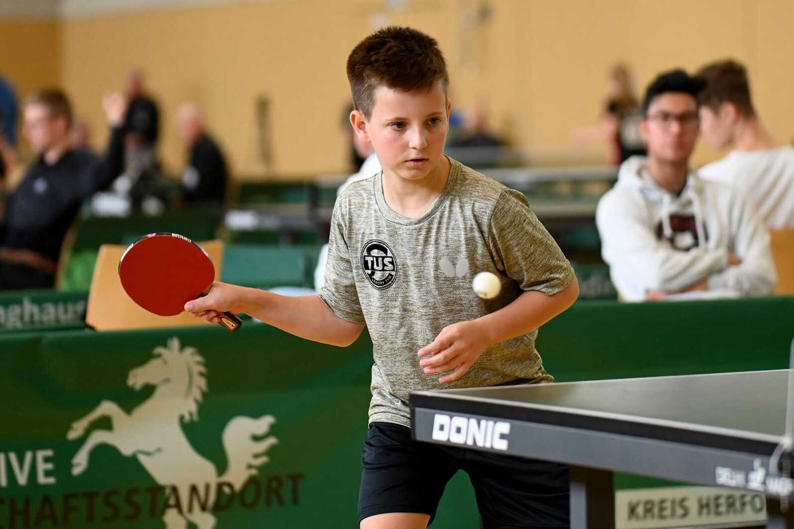 Ein junger Tischtennisspieler bereitet sich mit Schl&auml;ger und Ball auf einen Schlag an einem Tischtennistisch vor.