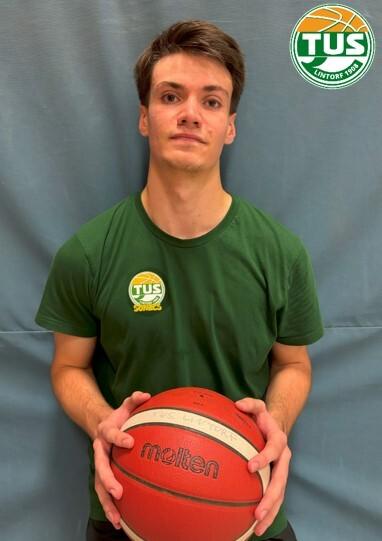 Junger Mann in gr&uuml;nem T-Shirt h&auml;lt einen Basketball vor einem blauen Hintergrund.