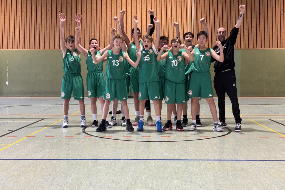 Gruppe jubelnder Basketballspieler in gr&uuml;nen Trikots steht auf einem Sportplatz und hebt die Arme in die Luft.