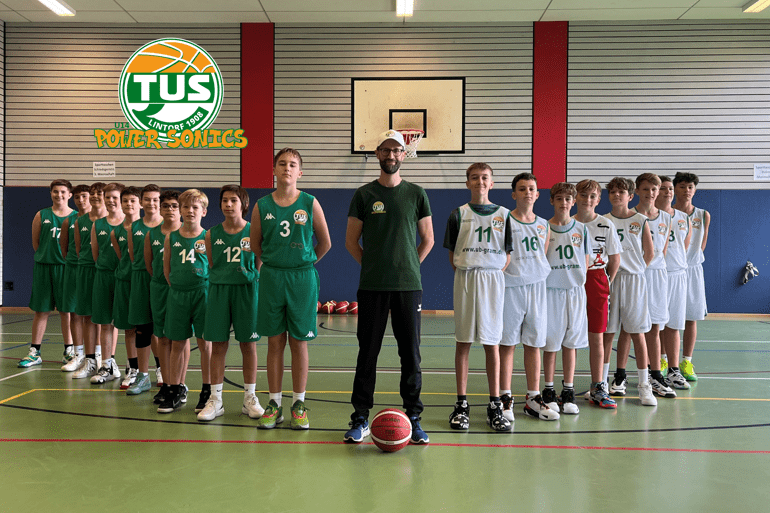 Gruppenshot von Basketballspielern in gr&uuml;nen und wei&szlig;en Trikots, aufgestellt in einer Sporthalle mit Basketballkorb.