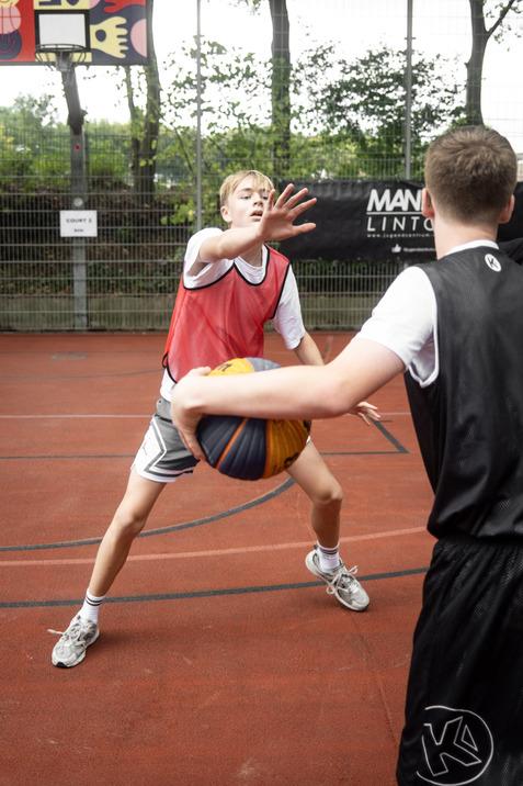 Zwei Jugendliche spielen Basketball auf einem Platz; einer verteidigt, w&auml;hrend der andere den Ball passt.