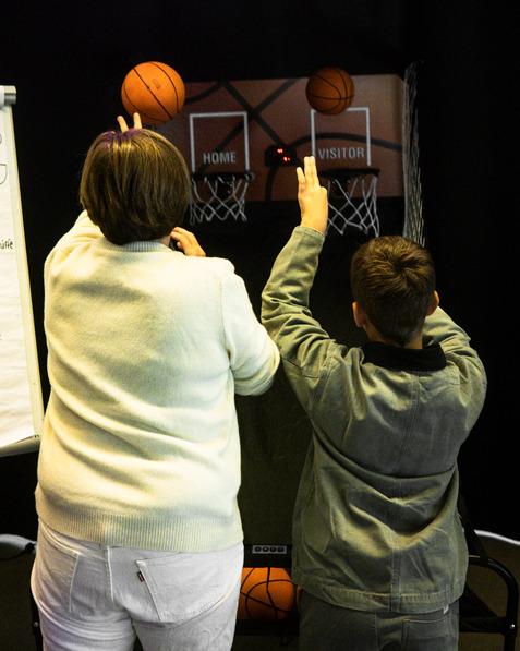 Frau und Junge werfen Basketballs in zwei K&ouml;rbe eines Spielger&auml;ts in einem dunklen Raum.