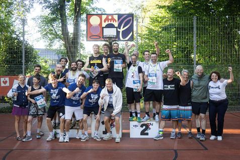 Gruppenshot von Sportlern auf dem Siegertreppe mit Medaillen und Pokalen nach einem Wettkampf im Freien.