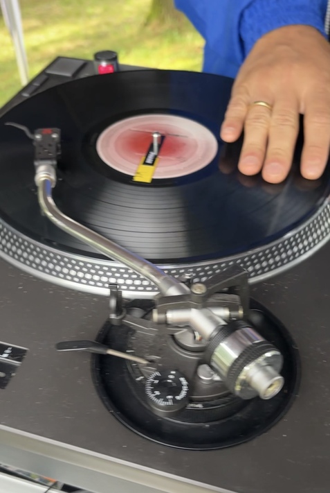 Hand eines DJs, die eine Schallplatte auf einem Plattenspieler anhebt, w&auml;hrend der Tonarm &uuml;ber der Platte schwebt.