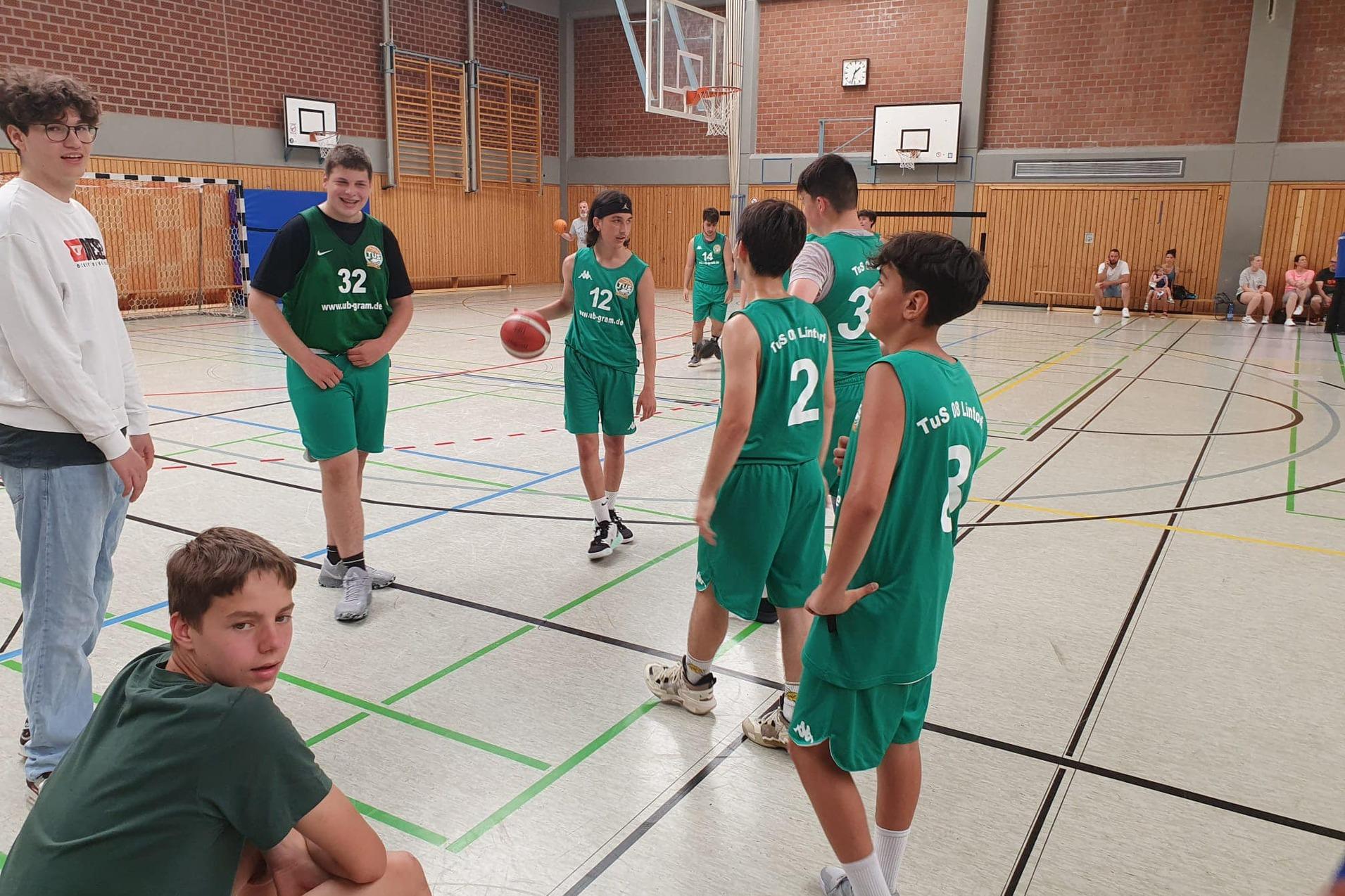 Sechs Jugendliche in grünen Basketballtrikots stehen in einer Sporthalle, einer hält den Ball in der Hand.