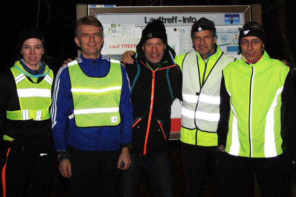 F&uuml;nf Personen in reflektierender Laufkleidung stehen vor einem Informationsschild f&uuml;r einen Lauftreff bei Nacht.