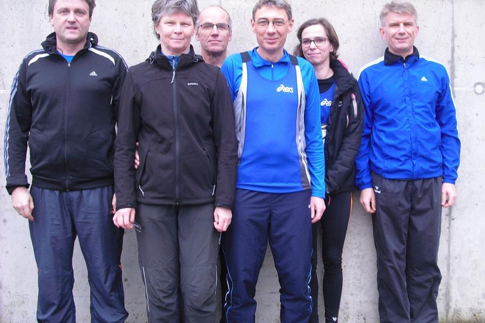 Sechs Personen in Sportbekleidung stehen vor einer grauen Wand. Sie l&auml;cheln und posieren f&uuml;r das Foto.