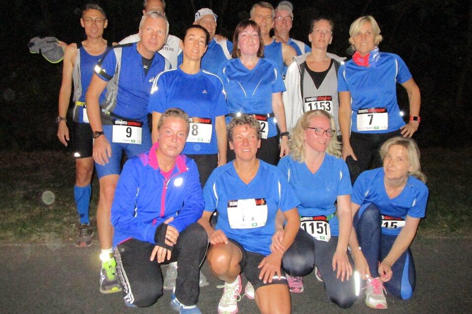 Gruppe von L&auml;ufern in blauen Trikots posiert fr&ouml;hlich nach einem Wettkampf bei D&auml;mmerlicht.
