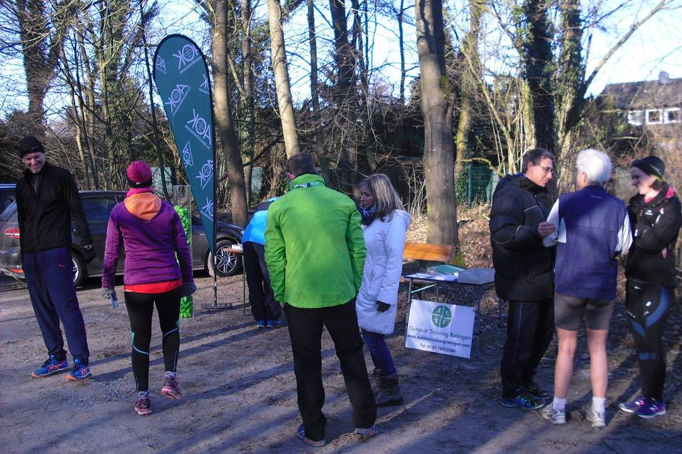 Gruppe von L&auml;ufern in Sportkleidung versammelt sich an einem Waldweg, mit Banner und Tischen im Hintergrund.