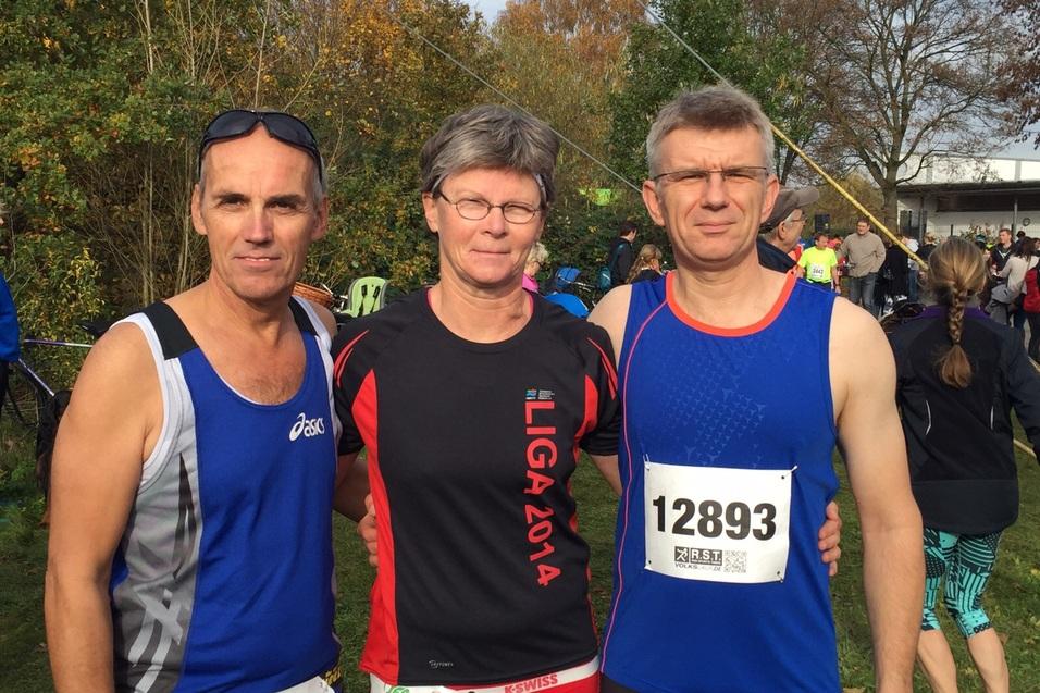 Drei L&auml;ufer stehen vor einer Veranstaltung im Freien, umgeben von bunten Sportlern und herbstlicher Natur.