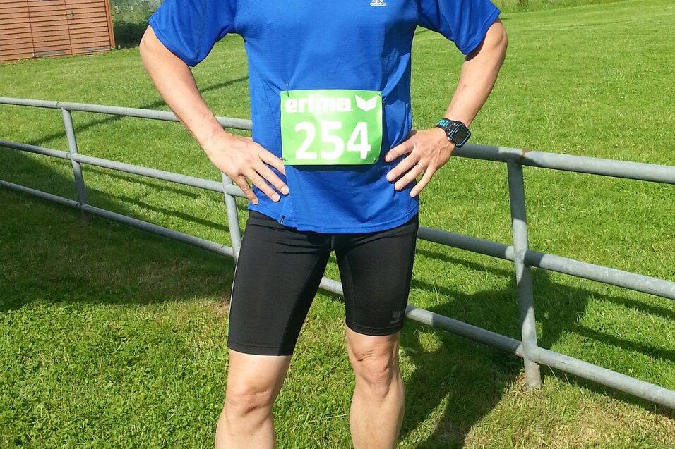 L&auml;ufer steht auf gr&uuml;ner Wiese, tr&auml;gt blaue Sportbekleidung und eine Startnummer 254, im Hintergrund B&auml;ume und Holzh&uuml;tte.