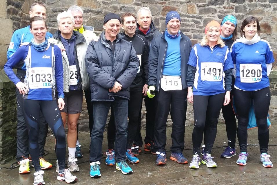 Gruppe von Laufteilnehmern in blauer Sportkleidung steht vor einer Steinmauer, bereit zum Wettkampf.