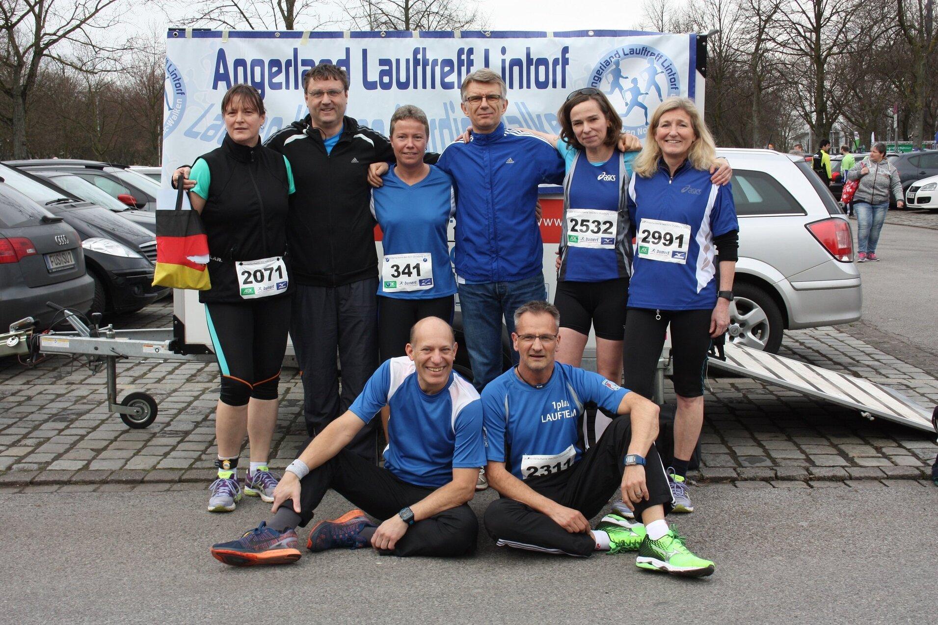 Gruppe von sieben Laufbegeisterten in Sportkleidung, posierend f&uuml;r ein Foto bei einer Veranstaltung im Freien.