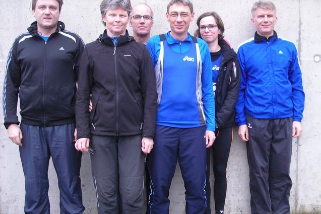 Sechs Personen in Sportbekleidung stehen vor einer grauen Wand. Sie l&auml;cheln und posieren f&uuml;r das Foto.