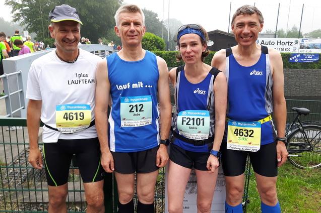 Vier L&auml;ufer stehen bei einem Wettkampf, gekleidet in Sportbekleidung und mit Startnummern, vor einem Zaun.