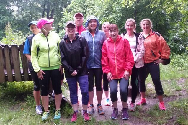 Gruppenaufnahme von acht Personen in Regenjacken, die auf einem schmalen Weg in einem gr&uuml;nen Wald stehen.