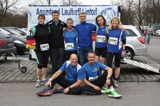 Gruppe von sieben Laufbegeisterten in Sportkleidung, posierend f&uuml;r ein Foto bei einer Veranstaltung im Freien.