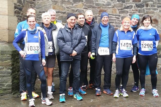 Gruppe von Laufteilnehmern in blauer Sportkleidung steht vor einer Steinmauer, bereit zum Wettkampf.