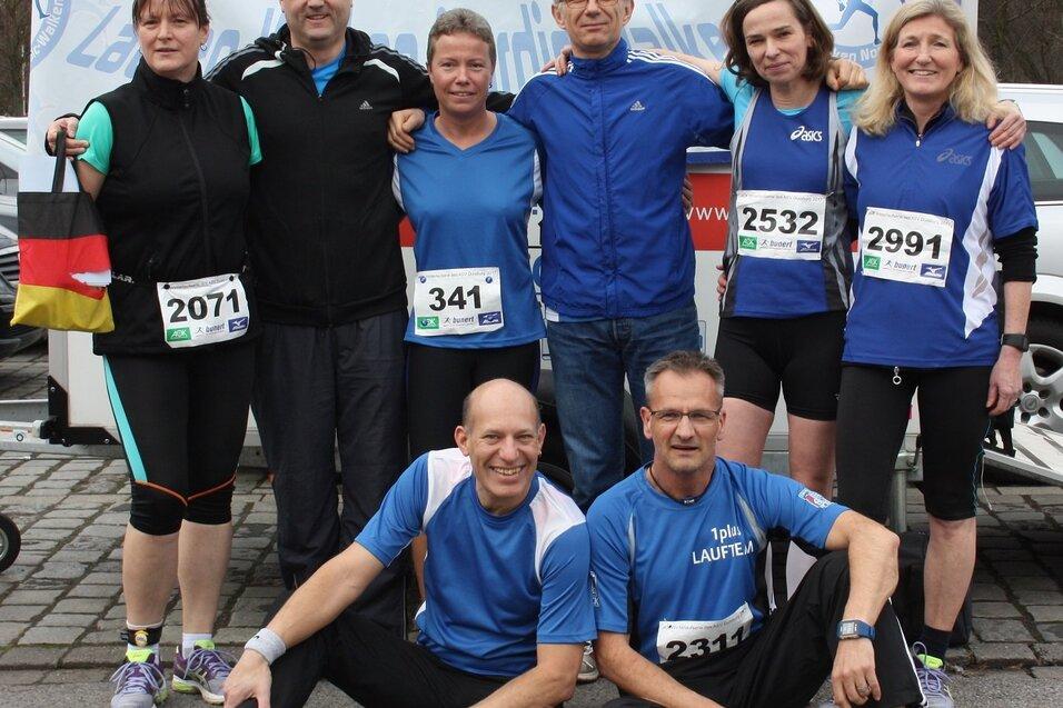 Gruppe von sieben Laufbegeisterten in Sportkleidung, posierend f&uuml;r ein Foto bei einer Veranstaltung im Freien.